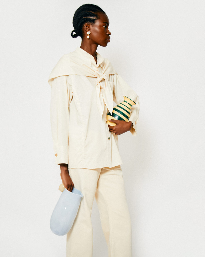 Model wears the off-white Jolene Blouse whilst holding the yellow and green Striped Vase from All'Origine